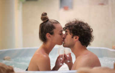 A couple shares a romantic moment in a hot tub with champagne in hand.