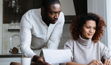 A couple organizes wedding details together while reviewing documents and planning online.