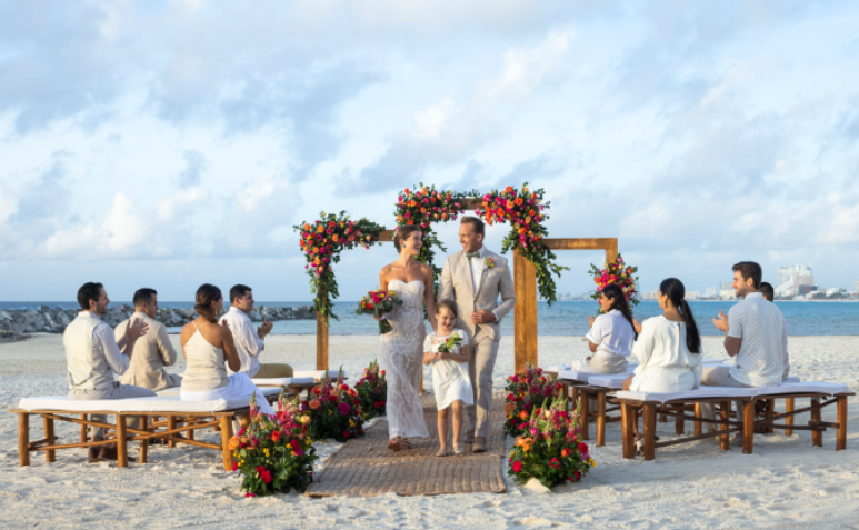 A couple walks down the aisle after their beachfront ceremony, surrounded by vibrant florals and loved ones.