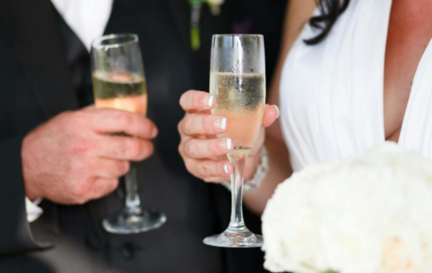 Close-up of bride and groom holding champagne glasses during wedding toast celebration.