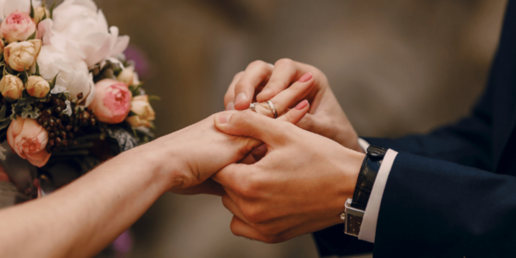 Close-up of a groom placing a wedding ring on the bride’s finger during a romantic ceremony, with a soft-focus bridal bouquet in the background.