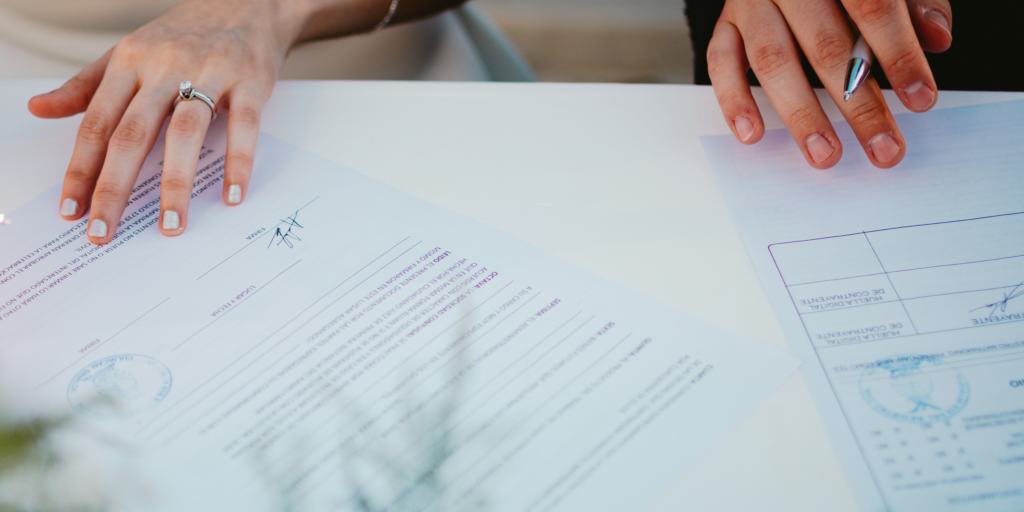 Couple signing marriage license paperwork at a desk during wedding planning process