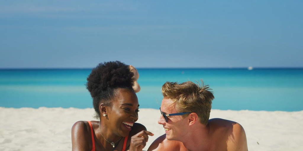 Couple smiling and relaxing together on a sunny tropical beach with turquoise ocean water.