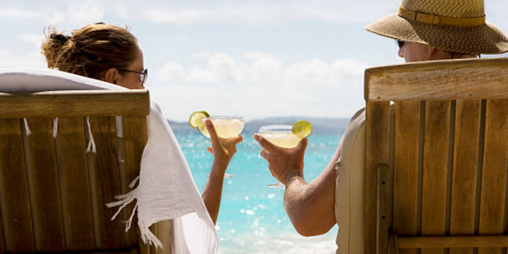 Couple relaxing in beach chairs holding margaritas while overlooking a tropical ocean view.