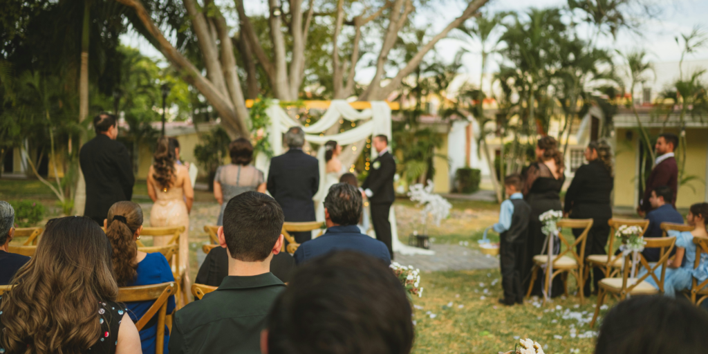 Outdoor garden wedding ceremony with couple exchanging vows under draped arch and seated guests.