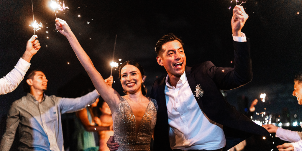 Newlywed couple celebrating with guests holding sparklers during wedding reception