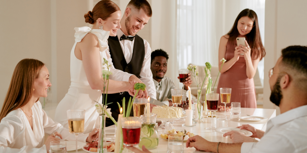 Newlywed couple cutting wedding cake during an intimate reception dinner with guests