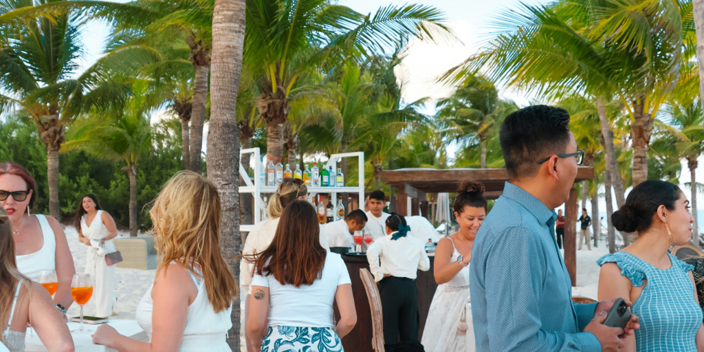 Guests enjoying a beachside wedding reception with drinks under palm trees at a tropical resort
