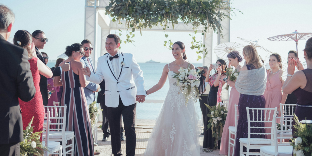 Bride and groom walking down the aisle after a beachfront wedding ceremony with ocean backdrop