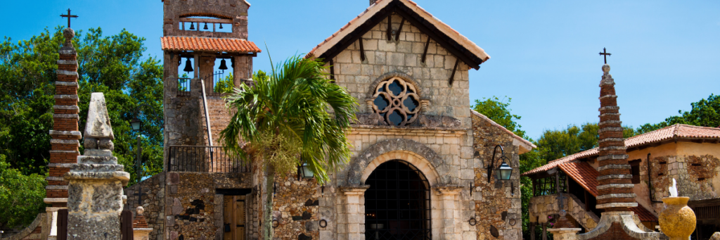 Historic stone chapel with bell towers and tropical landscaping in the Dominican Republic.