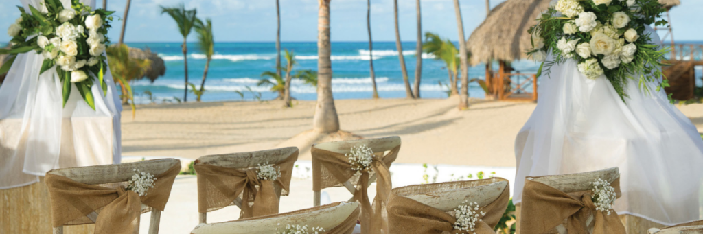 Beach wedding ceremony setup with white flowers, palm trees, and turquoise water in the Dominican Republic.