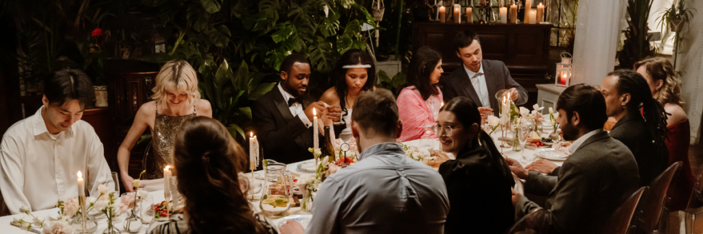 Intimate wedding dinner with guests gathered around a long candlelit table surrounded by lush greenery.